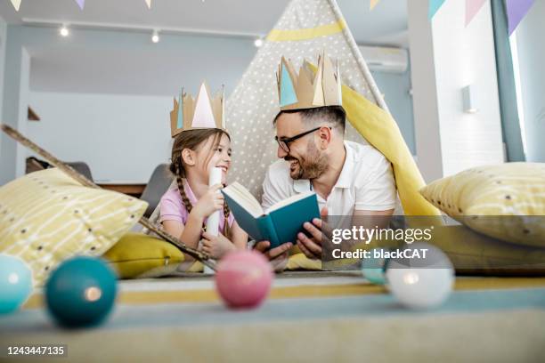 father is reading a book to the daughter - camping indoors stock pictures, royalty-free photos & images