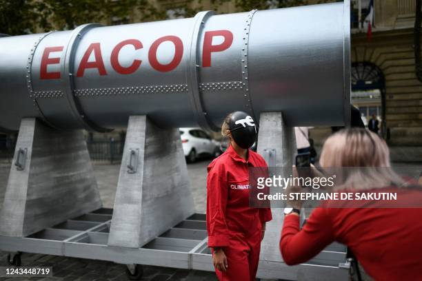 An activist wearing a Squid Game costume with "TE" written on the mask for Total Energies poses next to a fake EACOP pipeline structure during an...