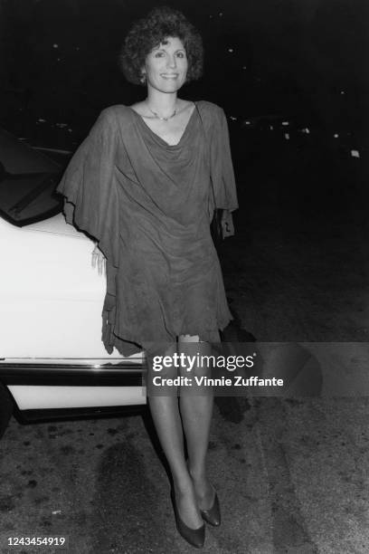 American actress and singer Lucie Arnaz, wearing a dress with a cowl neckline, poses beside a car as she attends the 60th Annual Academy Awards, held...