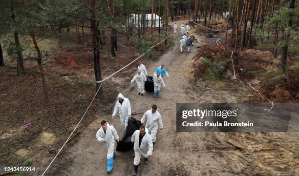 In an aerial view, rescue workers and forensic police carry exhumed bodies from unidentified makeshift graves at the Pishanske cemetery on September...