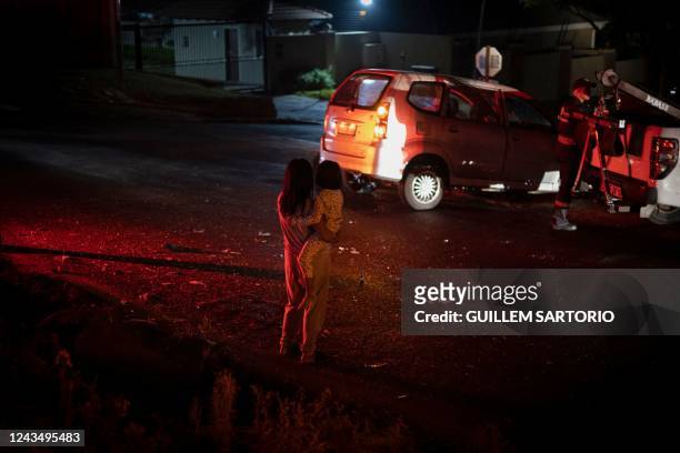 Woman holding a child who's just been in a car accident looks at a car being towed as paramedics help the injured during a night shift on payday...
