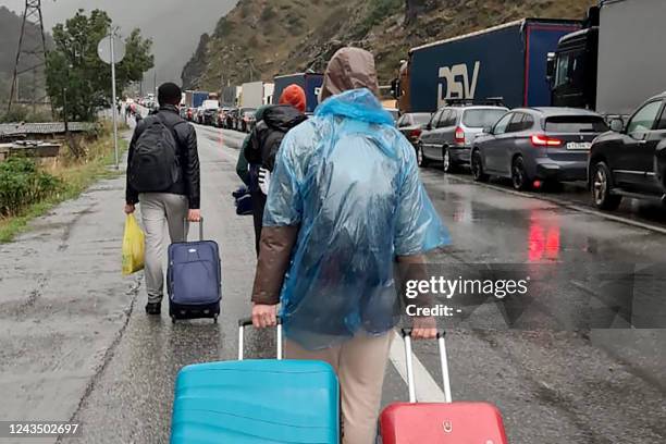 People carrying luggage walk past vehicles with Russian license plates on the Russian side of the border towards the Nizhniy Lars customs checkpoint...