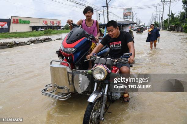 Residents commute on a tricycle loaded with their belongings along a flooded highway while evacuating from their submerged homes in the aftermath of...