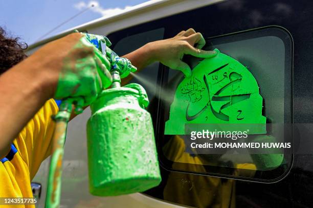 Boy sprays a stencil cutout depicting the Muslim Prophet Mohamed's name in Arabic calligraphy on green dome of the Masjid al-Nabawi , which is in the...