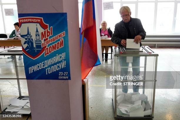 Man casts his ballot for a referendum at a polling station in Mariupol on September 27, 2022. The placard reads "Referendum. We are returning home....
