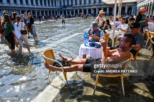 Tourists sit at a cafe's terrace on a flooded St. Mark's square in Venice on September 27 following an "Alta Acqua" high tide event, too low to...