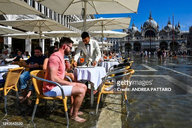 Tourists get their drinks served at a cafe's terrace on a flooded St. Mark's square in Venice on September 27 following an "Alta Acqua" high tide...