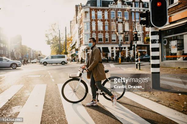 hombre con máscara facial empujando bicicleta en la ciudad durante el bloqueo de la pandemia de coronavirus - netherlands fotografías e imágenes de stock