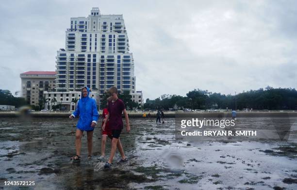 People walk along the mudflats as the tide recedes from Tampa Bay ahead of Hurricane Ian making landfall on September 28, 2022 in Tampa, Florida. -...