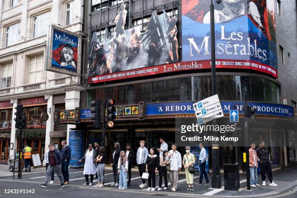 People wait to cross the street underneath poster for Les Miserables at the Sondheim Theatre on Shaftesbury Avenue, at the heart of Londons...