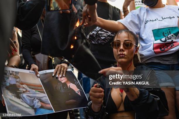 Protestors set fire to material as they hold banners with the portrait of Iranian Mahsa Amini while they take part in a rally outside the Iranian...