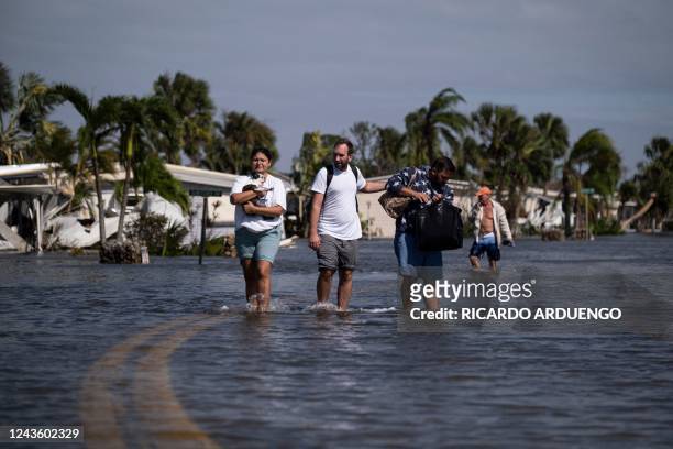 People carry their belongings wade through water on a flooded neighborhood in the aftermath of Hurricane Ian in Fort Myers, Florida on September 29,...