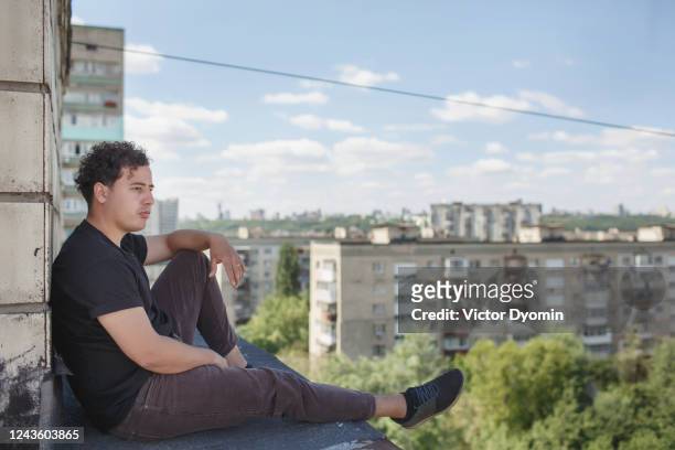 young man is sitting alone on the roof - altitude sickness stock pictures, royalty-free photos & images