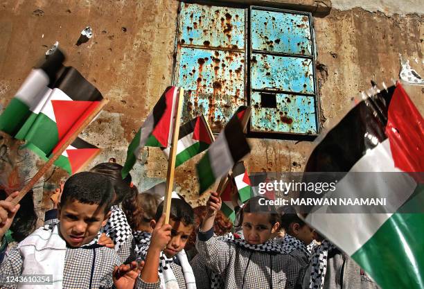 Palestinian children wave their national flags in front of a bullet-riddled wall during a demonstration in the refugee camp of Burj al-Barajneh in...