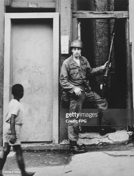 Young African American boy passes a National Guardsman in an alley of Springfield Avenue during a period of rioting in Newark, New Jersey, July 1967.