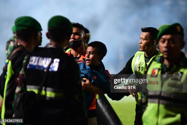 This picture taken on October 1, 2022 shows a boy being carried as members of the Indonesian army secure the pitch after a football match between...