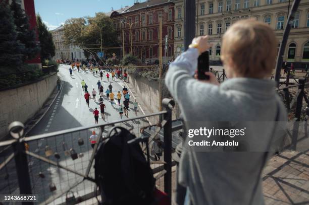 Woman is taking photographs with her mobile phone as runners of the 99th Kosice Peace Marathon are going past below a bridge in Kosice, Slovakia on...