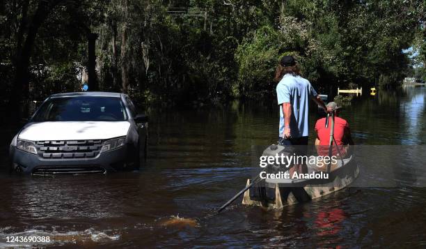 Two men motor a boat past a stranded car to pick up items from a home that was flooded by rain from Hurricane Ian on October 1, 2022 in Orlando,...