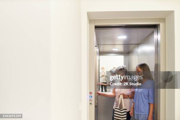 a grandmother and her daughter are standing in an elevator that a young man wants to ride in during the corona crisis, they are all worried about the distance - social distancing elevator stock pictures, royalty-free photos & images