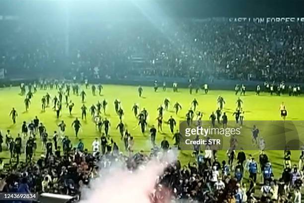 This screengrab of an AFPTV video taken on October 1, 2022 shows tear gas in the crowd as people run on the pitch after a football match between...