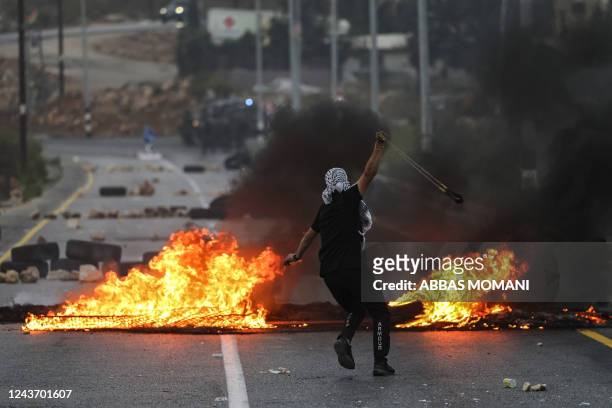 Palestinian youth throws a rock with a slingshot at Israeli security forces during clashes at the northern entrance of the city of Ramallah in the...