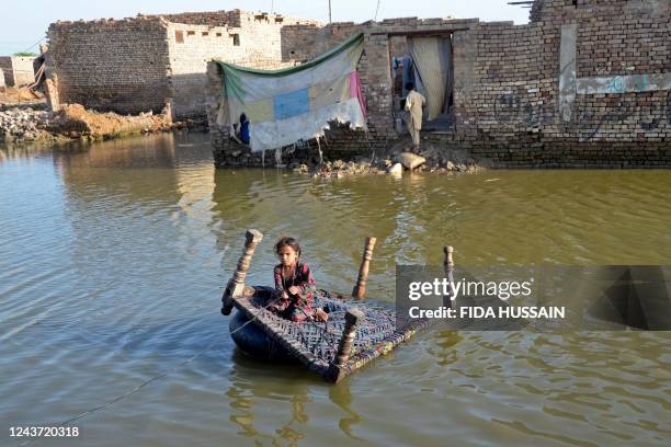 Girl sits on a cot as she crosses a flooded street at Sohbatpur in Jaffarabad district of Balochistan province on October 4, 2022.