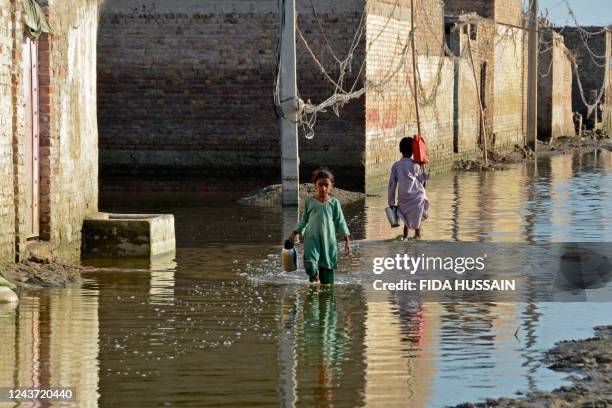 Children carry water pots as they wade through a flooded street at Sohbatpur in Jaffarabad district of Balochistan province on October 4, 2022.