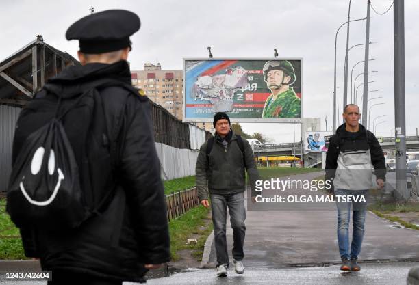 Men walk past a billboard promoting contract army service in Saint Petersburg on October 5, 2022. - Russian President Vladimir Putin announced on...