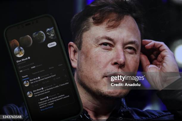 In this photo illustration, Elon Musk's twitter profile is displayed on a mobile phone and the image of him is seen on a computer screen on back of...