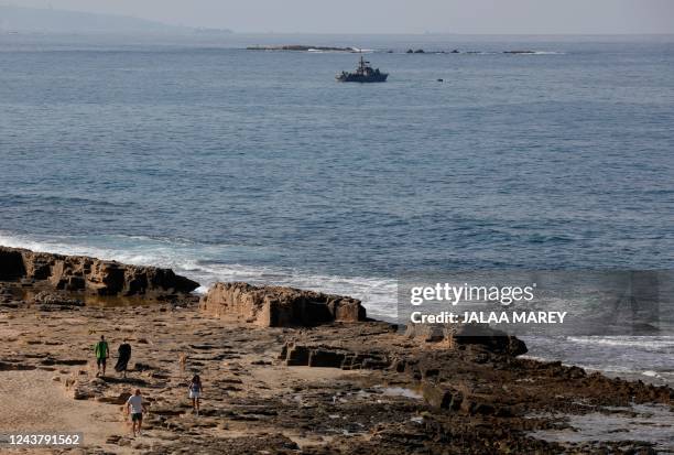 People walk along the beach as a navy vessel patrols the Mediterranean waters off Rosh Hanikra, known in Lebanon as Ras al-Naqura, on the Israeli...