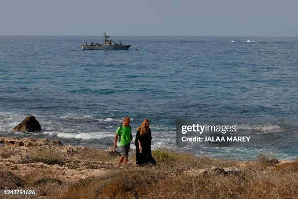 People walk along the beach as a navy vessel patrols the Mediterranean waters off Rosh Hanikra, known in Lebanon as Ras al-Naqura, on the Israeli...