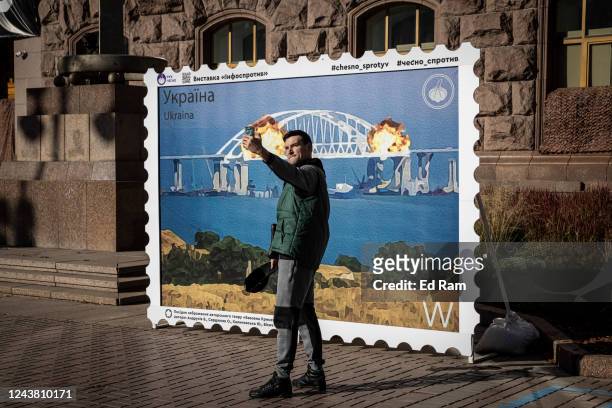 People pose for photographs in front of a picture of a postage stamp showing an artists impression of the Kerch bridge on fire on October 8, 2022 in...
