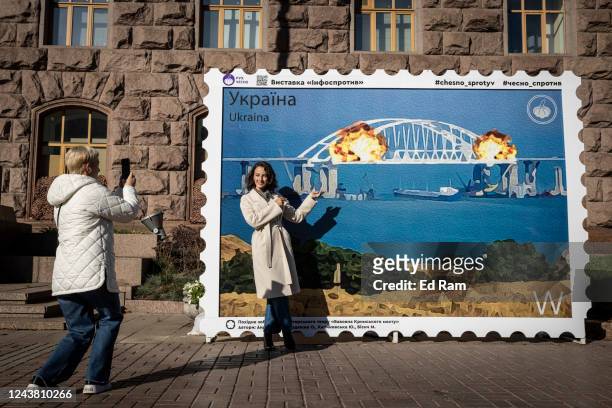 People pose for photographs in front of a picture of a postage stamp showing an artists impression of the Kerch bridge on fire on October 8, 2022 in...