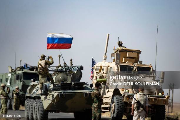 Soldiers of a Russian military convoy and their US counterparts exchange greetings as their patrol routes intersect in an oil field near Syria's...