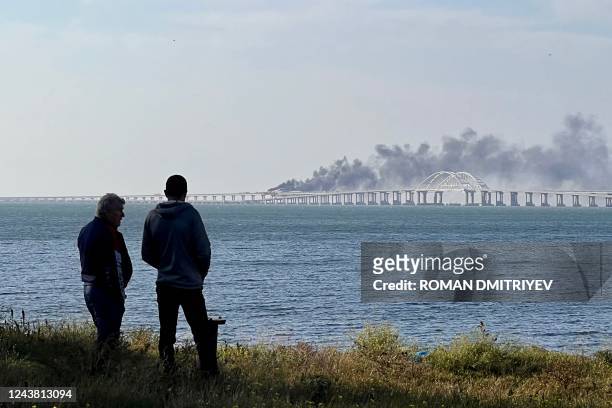 People look at thick black smoke rising from a fire on the Kerch bridge that links Crimea to Russia, after a truck exploded, near Kerch, on October...