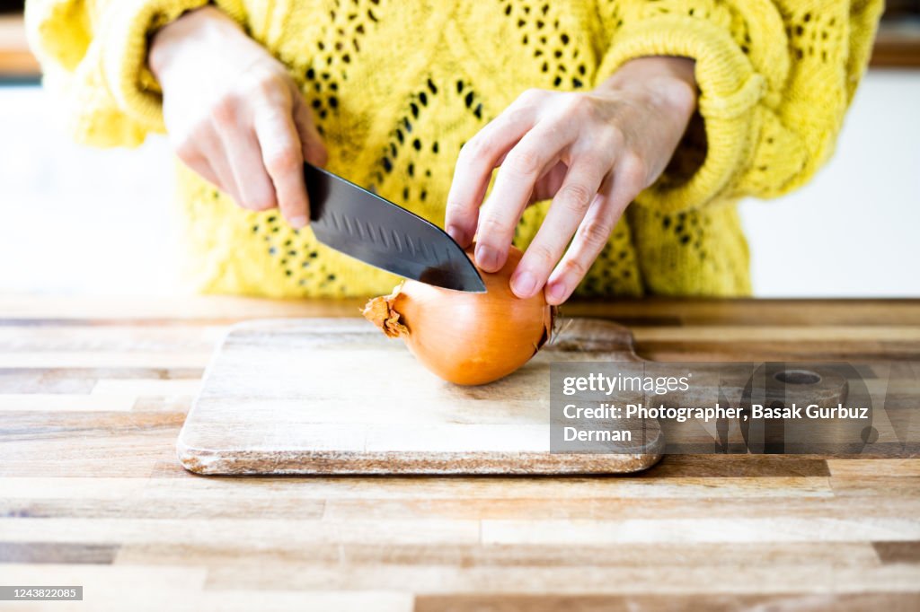 A woman chopping onions with a kitchen knife on wooden cutting board