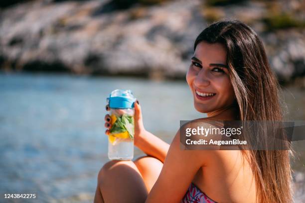 donna carina che beve acqua detox in spiaggia - alcohol detox foto e immagini stock