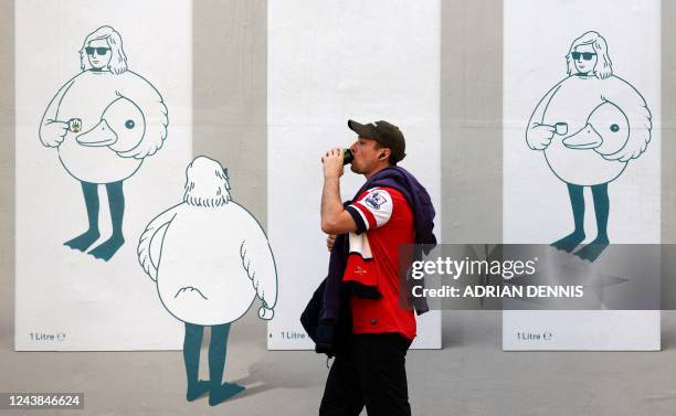 An arsenal fan walks past an advert for oat milk as they arrive ahead of the English Premier League football match between Arsenal and Liverpool at...