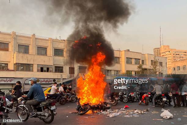 Picture obtained by AFP outside Iran, shows people gathering next to a burning motorcycle in the capital Tehran on October 8, 2022. - Iran has been...