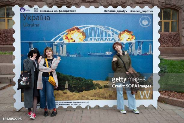 People pose for a photo with a stamp model depicting the burning Crimean bridge in the background, in central Kyiv. On October 8, an explosion...