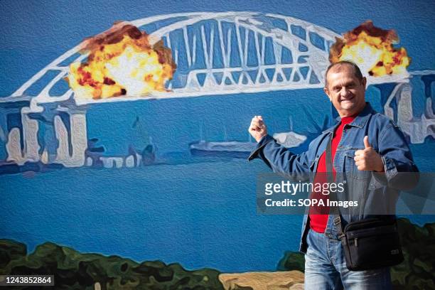 Man poses for a photo with a stamp model depicting the burning Crimean bridge in the background, in central Kyiv. On October 8, an explosion occurred...