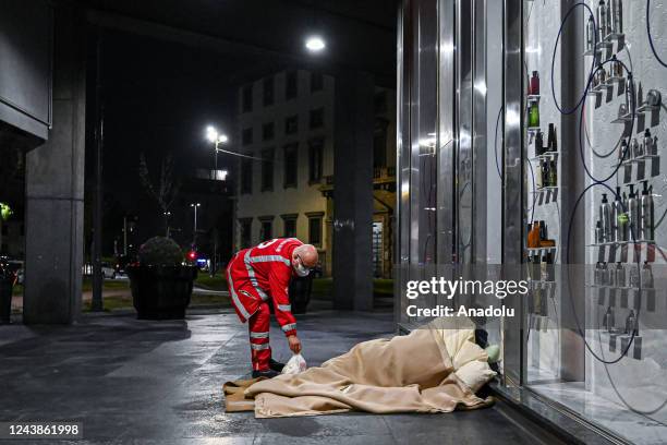 Volunteer of Croce Rossa Italiana leaves a bag of food to a man sleeping under a blanket while giving assistance to homeless people in Milan, Italy...