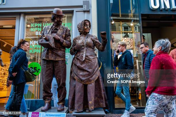 People are seen passing by behind of a couple performing as living statues. The World Living Statues Festival has evolved in thirteen years into the...