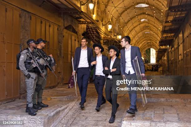 Israeli policemen stand on guard as ultra-Orthodox Jewish men walk along a market alley in the old city of Jerusalem during the Jewish holiday of...