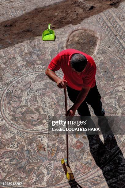 Man sweeps dirt with a broom off of a mosaic floor dating to the Roman era being excavated in the city of al-Rastan in Syria's west-central province...