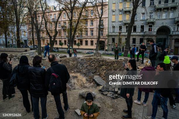 People gather by a rocket crater in a park of central Kyiv on October 12 two days after Ukraine's capital was hit by multiple Russian strikes, the...
