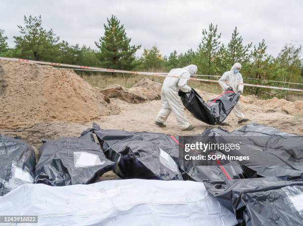 Investigators are seen carrying a body bag with a Ukrainian soldier's body which was exhumed from a burial site in Lyman. At least 32 Ukrainian...