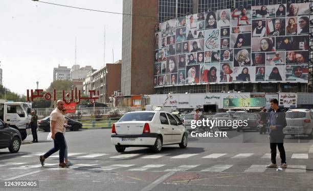 Iranians drive past a huge billboard showing a montage of pictures titled "the women of my land, Iran" featuring Iranian women who are all observing...