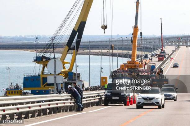 This picture taken on October 13, 2022 shows workers restoring damaged parts of the Kerch Bridge that links Crimea to Russia, which was hit by a...