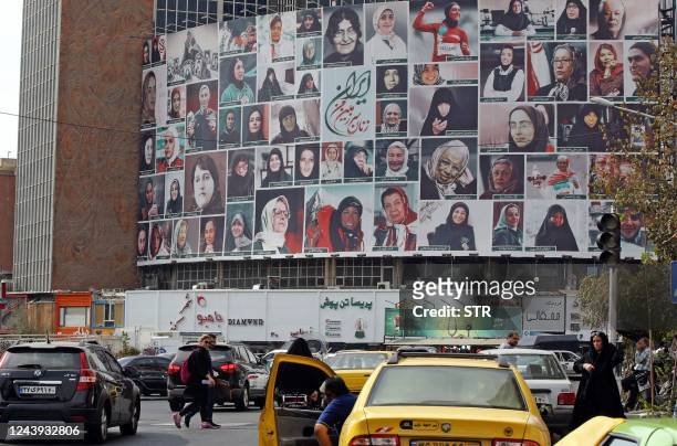 Iranians drive past a huge billboard showing a montage of pictures titled "the women of my land, Iran" featuring Iranian women who are all observing...
